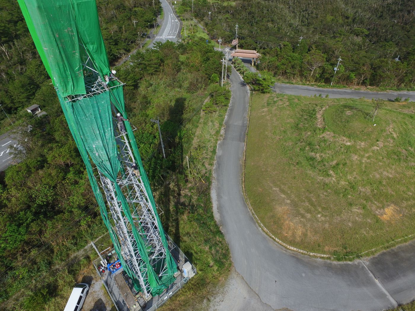 養生メッシュに覆われた鉄塔と麓の道路をドローンから見下ろした写真