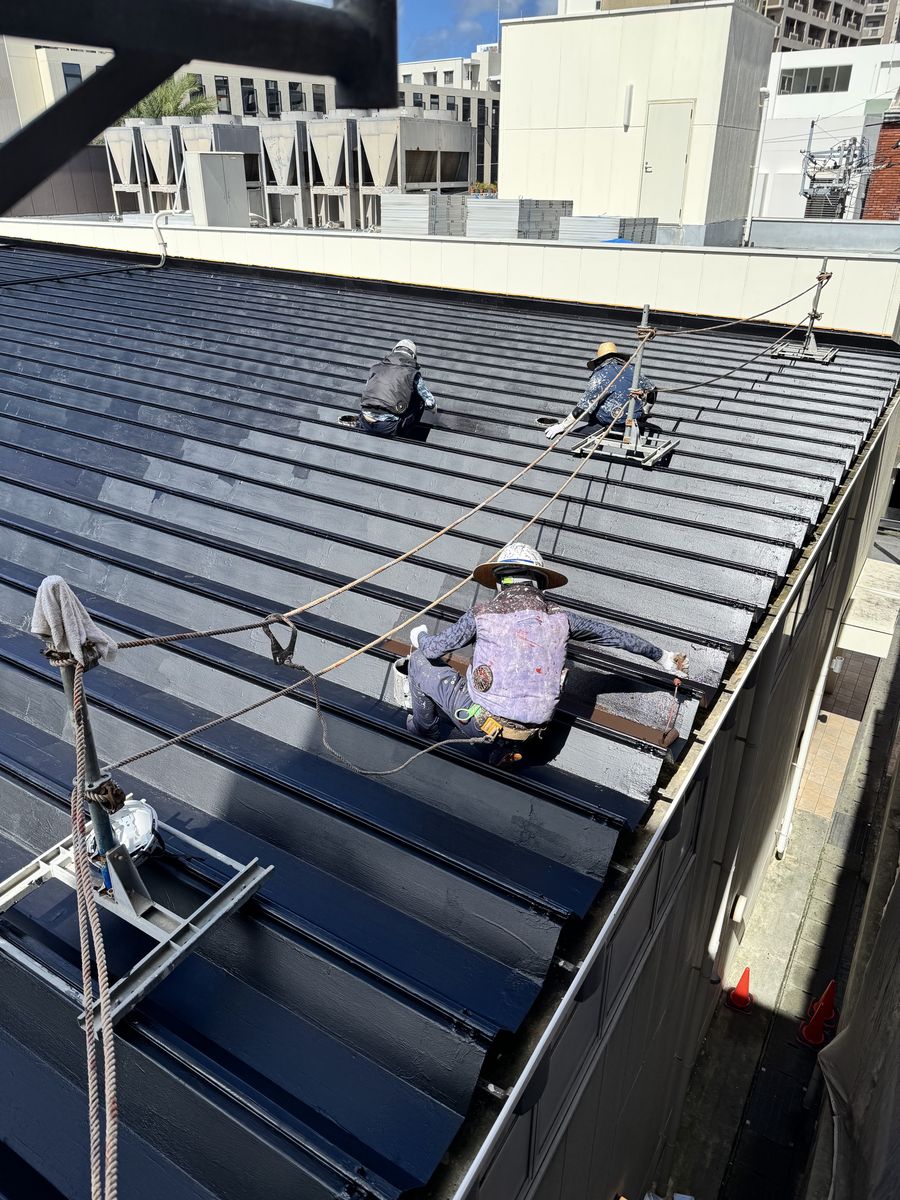 金属屋根の上で、命綱を着けて塗装作業を行う職人たち